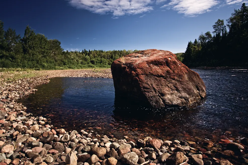 A great red boulder in Indian River on a summer afternoon, sun on the rock, clear water over the stones.