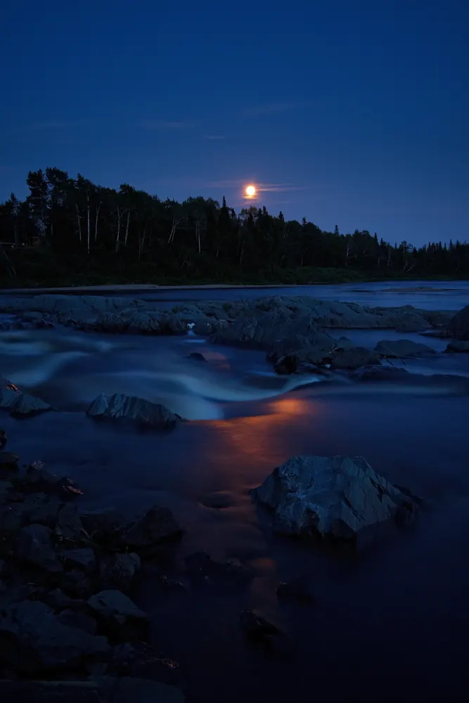 Indian River at night under a rising moon, water running white between dark rocks.